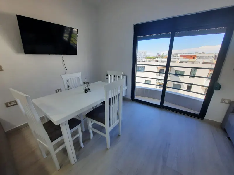 White dining table and chairs by the balcony with TV on the wall